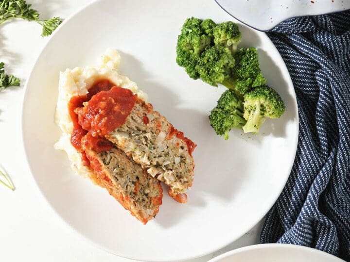Slices of meatloaf with mashed potatoes and broccoli on white plates