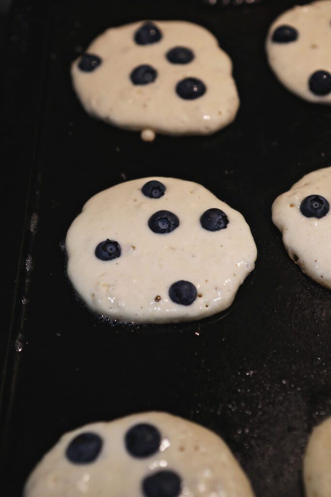 Blueberry pancakes cooking on a griddle