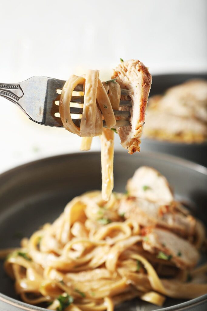 A fork holds a bite of chicken alfredo pasta