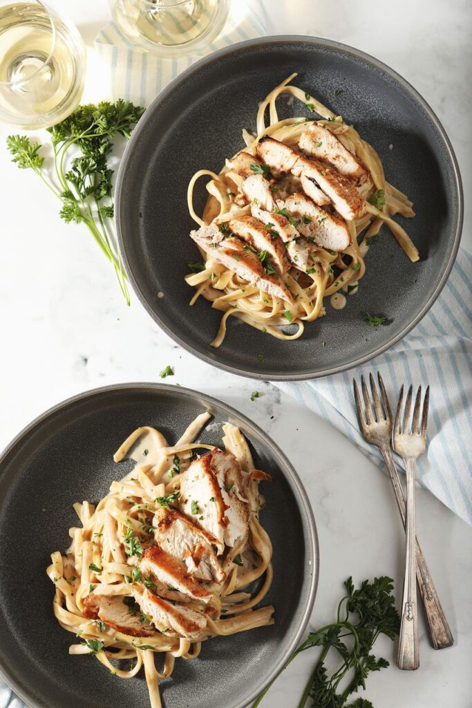 Two bowls of Cajun Chicken Alfredo with wine and forks