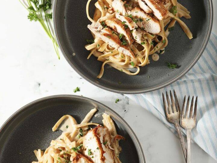 Two bowls of Cajun Chicken Alfredo with wine and forks