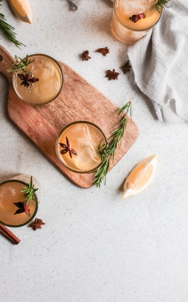 Three whiskey smashes from above on wood with rosemary, lemon and star anise