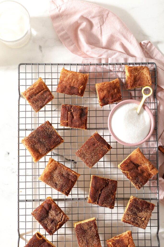 Sliced snickerdoodle bars on a cooling rack with a bowl of sugar