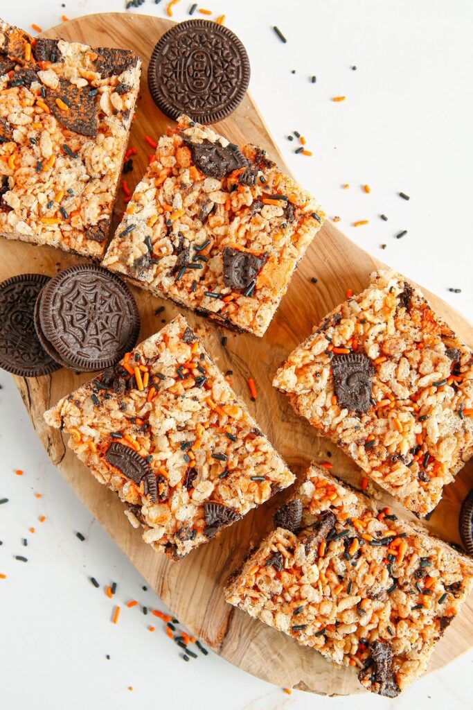 Orange and black crispy rice treats on a wooden board with cookies and sprinkles