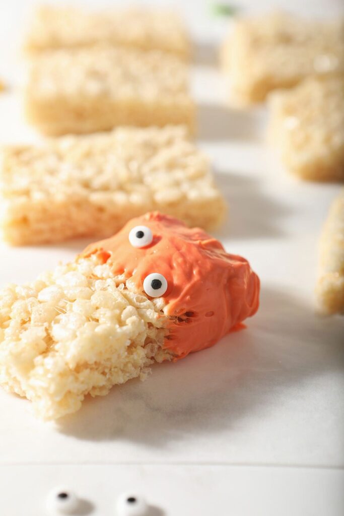 A rice krispie treat dipped in orange candy with candy eyeballs