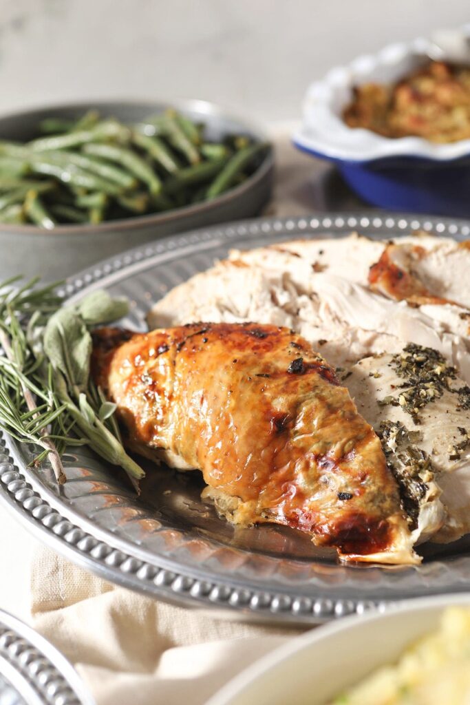 Sliced herb butter turkey breast on a tray with herbs