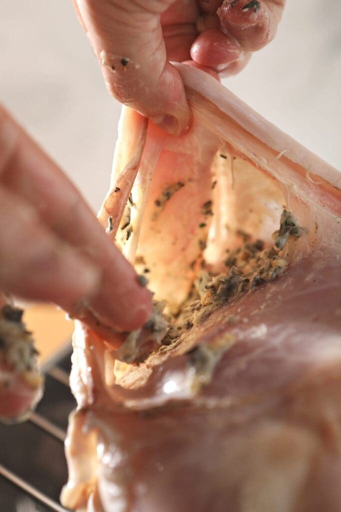 A hand rubs turkey butter beneath turkey skin