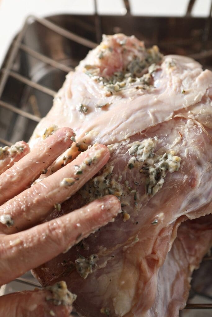 A hand rubs herb butter all over the exterior of a turkey breast