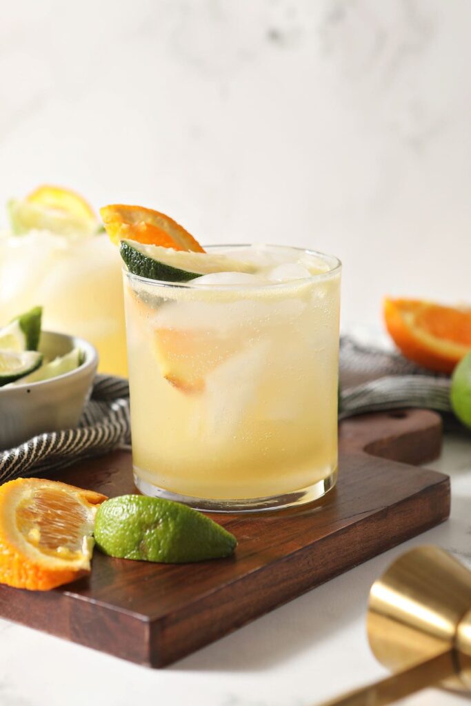 Two margarita mocktails with lime and orange wedges