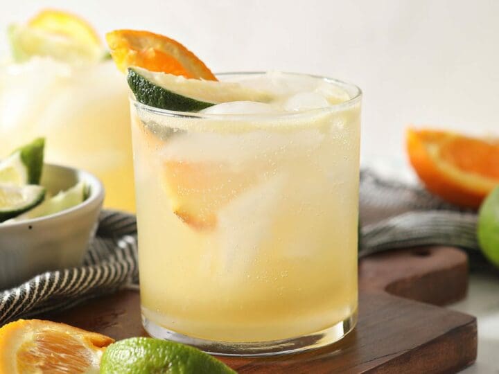 Two margarita mocktails with lime and orange wedges
