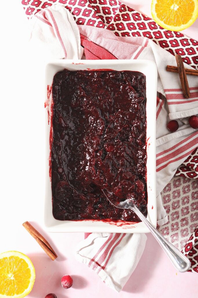 A spoon sits in a white casserole dish holding cranberry sauce