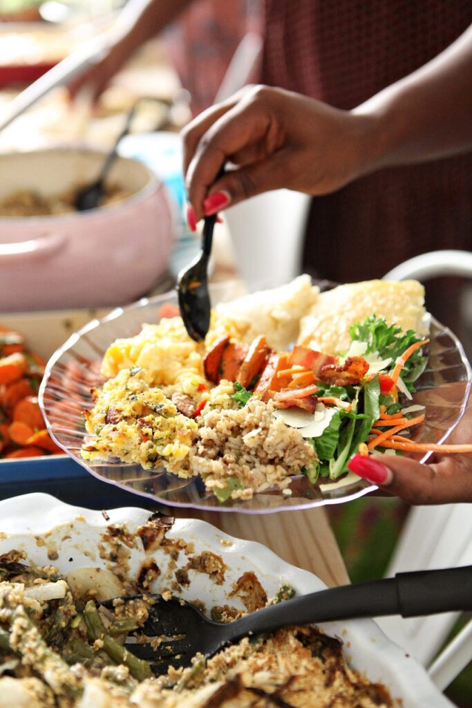 A woman scoops carrots onto a loaded plate at Friendsgiving