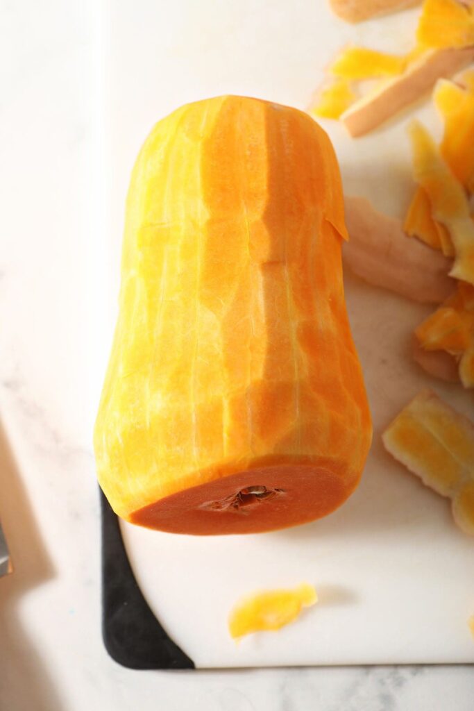 A peeled butternut squash on a white cutting board