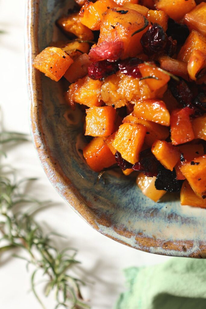 A blue pottery dish holds roasted Maple Cranberry Butternut Squash