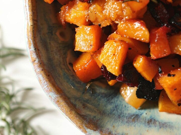A blue pottery dish holds roasted Maple Cranberry Butternut Squash