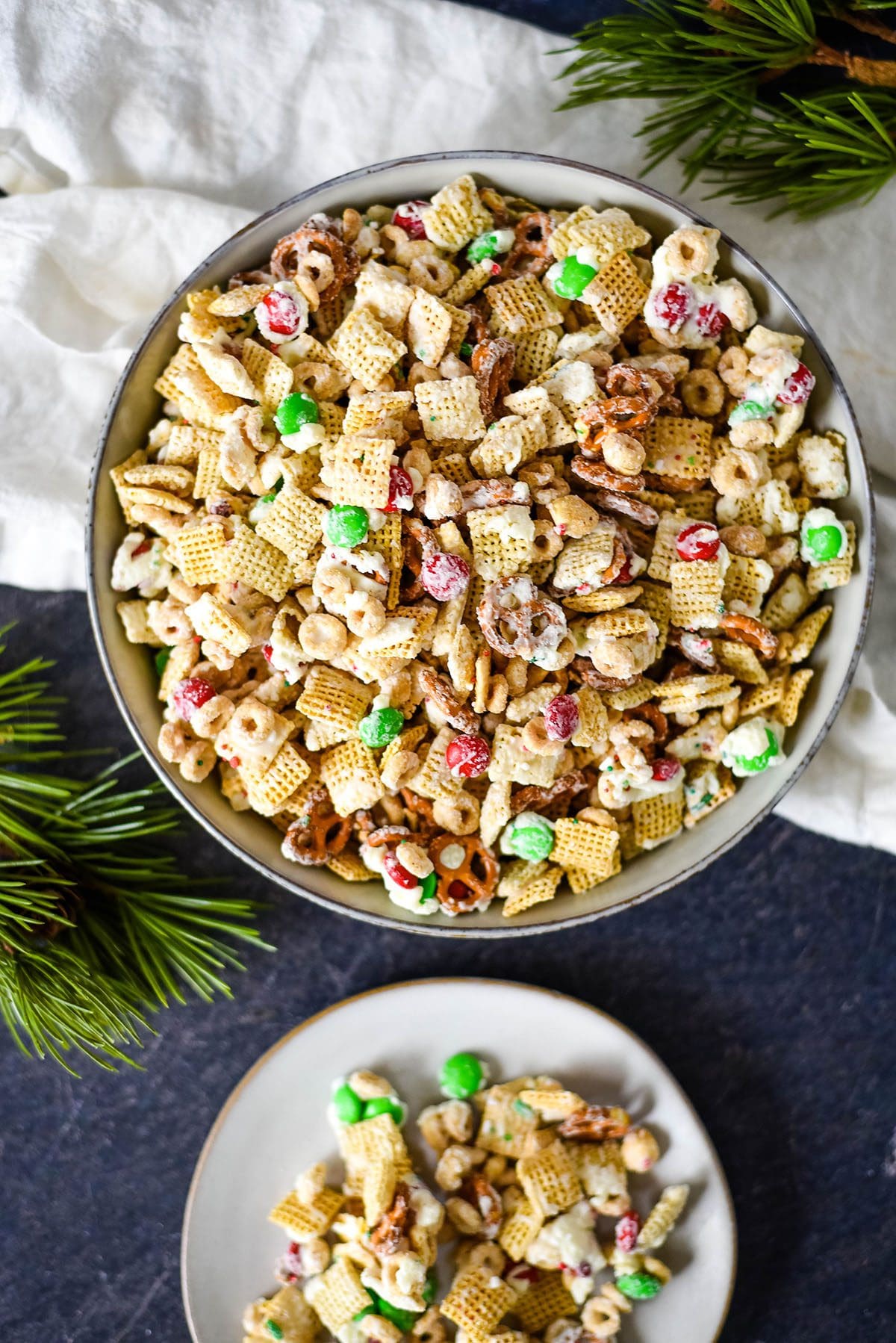 A bowl of Christmas Chex Mix with a serving on a plate