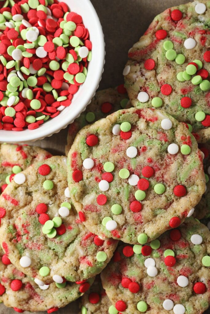 Several Christmas Confetti Cookies stacked near a bowl of sprinkles