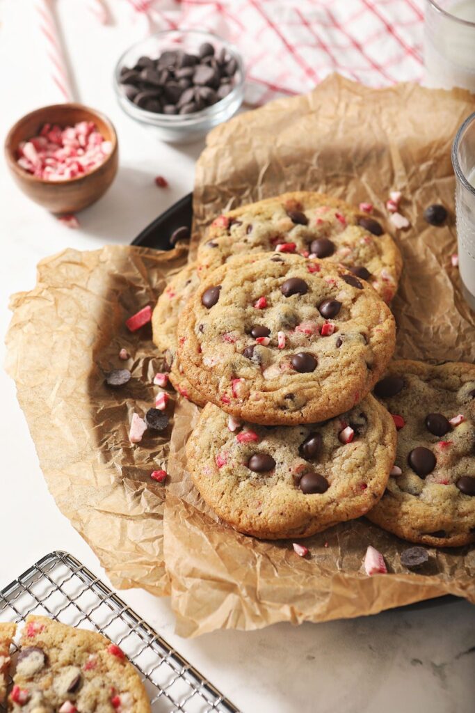 Stacked Peppermint Chocolate Chip Cookies on a plate with bowls of peppermint and chocolate