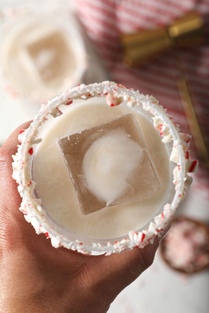 A hand holds a milky cocktail with a candy cane rim