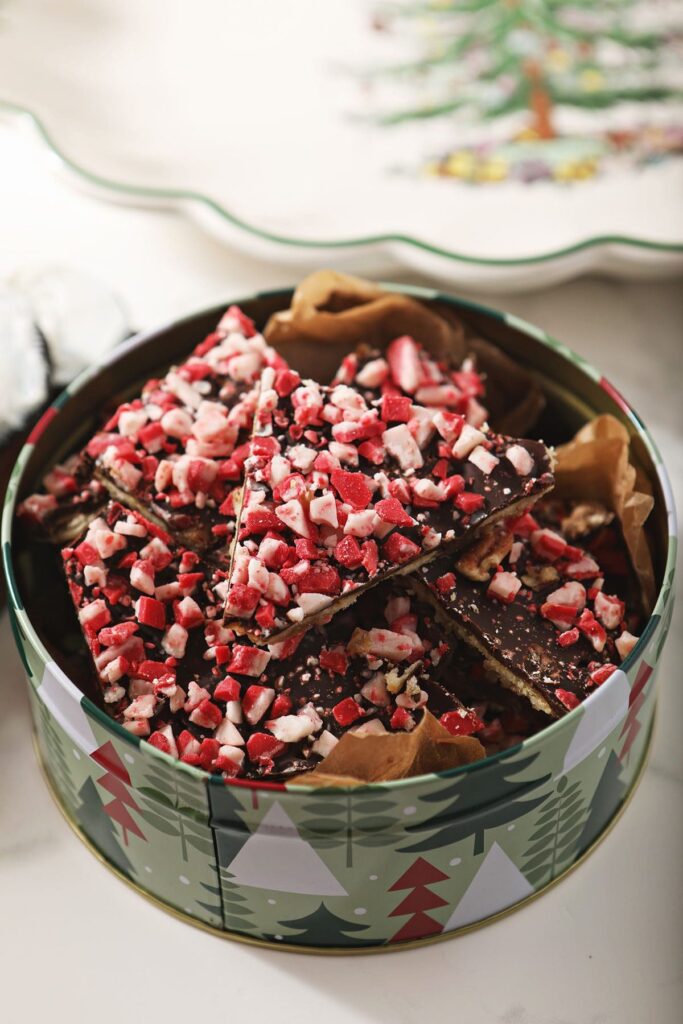 A tin of peppermint saltine cracker toffee by a christmas platter