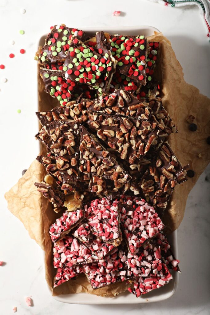 A platter of three different types of saltine cracker toffee with nuts, sprinkles and peppermint