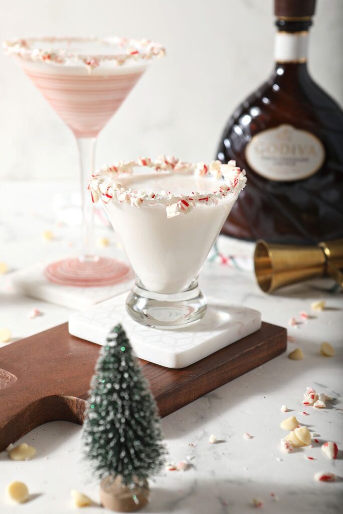 Two martini glasses with white chocolate martinis surrounded by candy canes and christmas decor