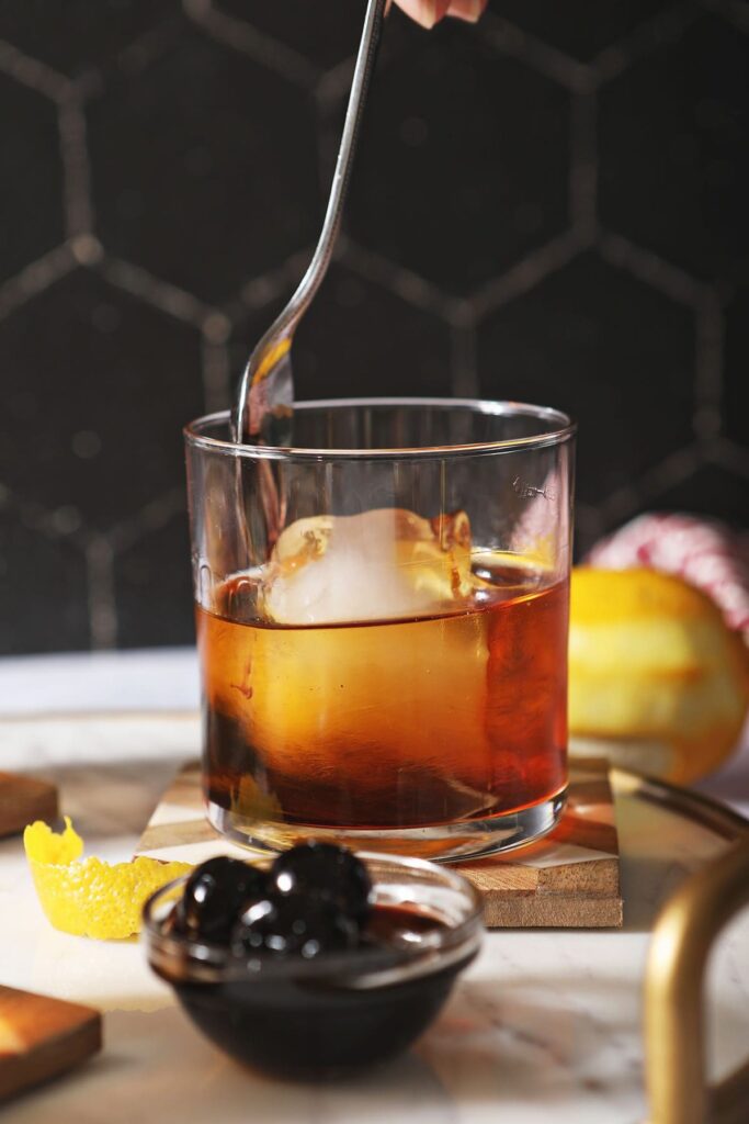 A spoon stirs an amaro cocktail with a huge ice cube