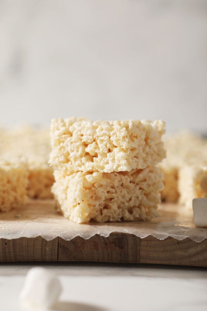 Two rice krispie treats are stacked on top of each other on a cutting board