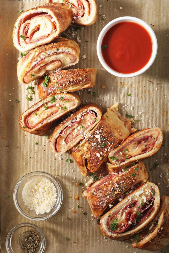 A sliced meat-filled stromboli on a sheet pan with tomato sauce and parmesan cheese