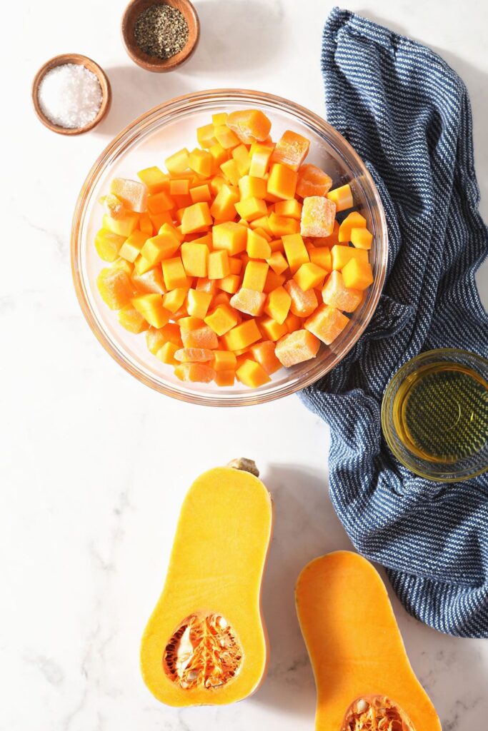 Butternut squash in a bowl and halved with ingredients in bowls