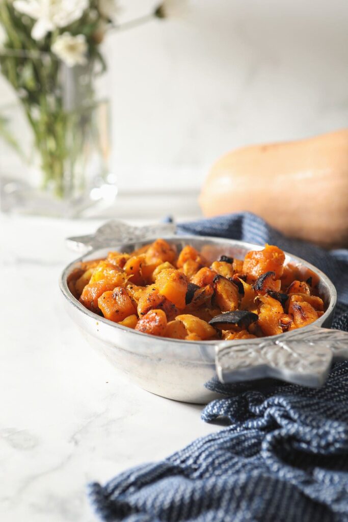 A silver bowl of roasted butternut squash on marble with a blue towel