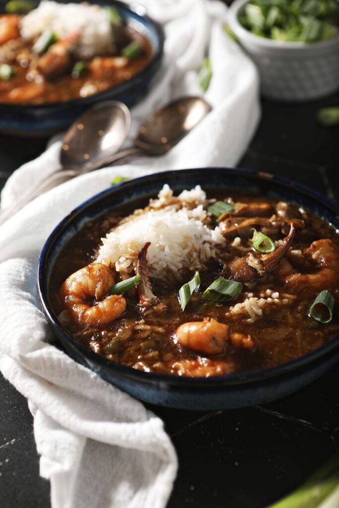 Two bowls of Seafood Gumbo on black tile with spoons and a white towel