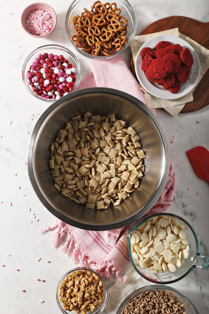 Bowls holding ingredients to make a holiday chex mix recipe on marble