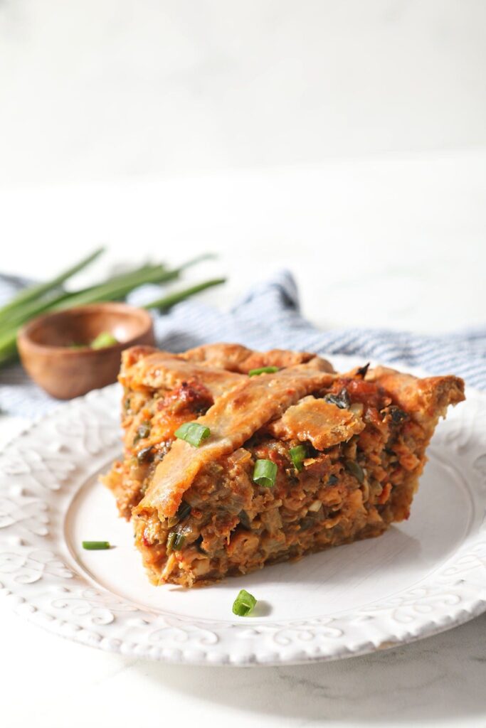 A slice of crawfish pie on a white plate by a blue striped towel