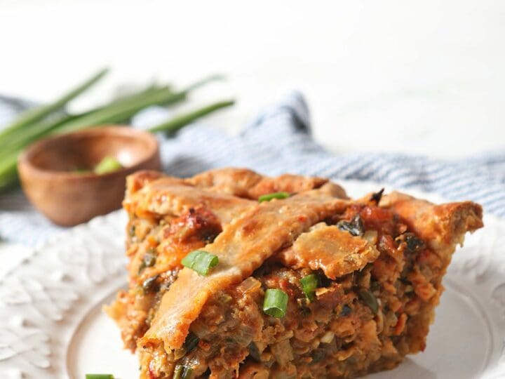 A slice of crawfish pie on a white plate by a blue striped towel