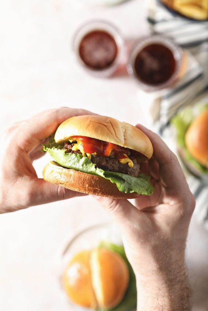 A man holds a burger in hand above a table