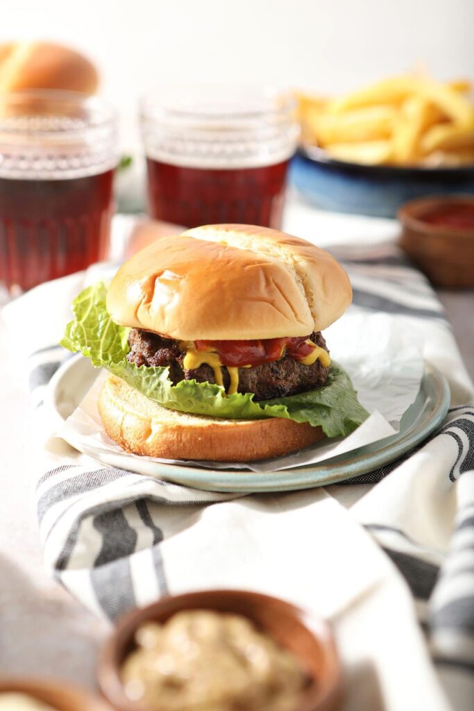 A pan fried hamburger on a plate next to beer glasses