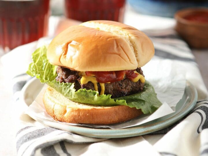 A pan fried hamburger on a plate next to beer glasses