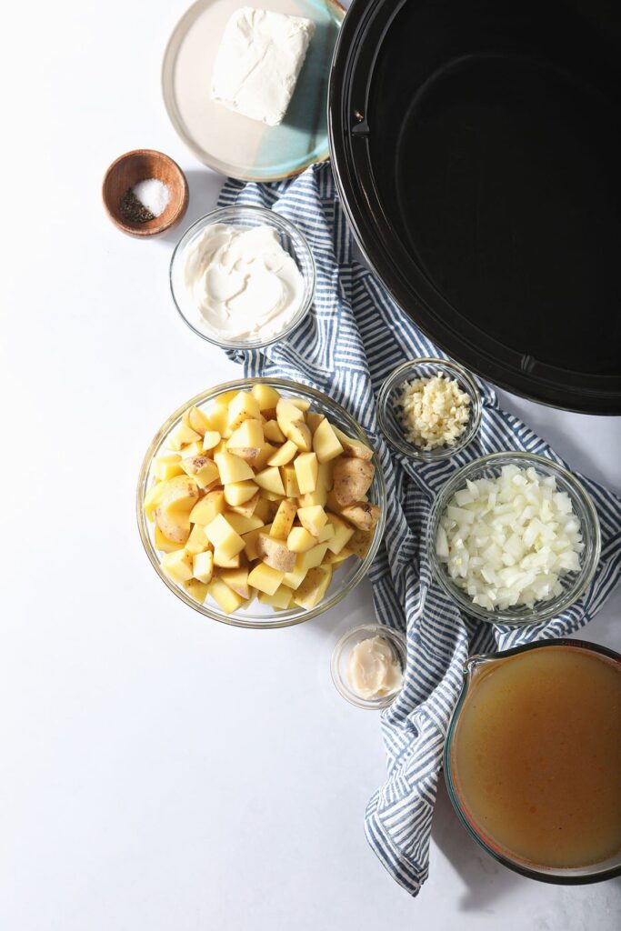 Potatoes and other ingredients in bowls next to a slow cooker