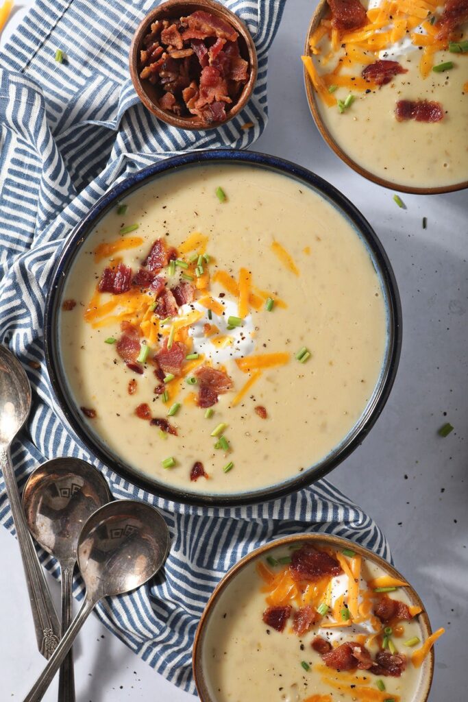 Three bowls of Slow Cooker Potato Soup garnished with bacon, cheese, sour cream and chives