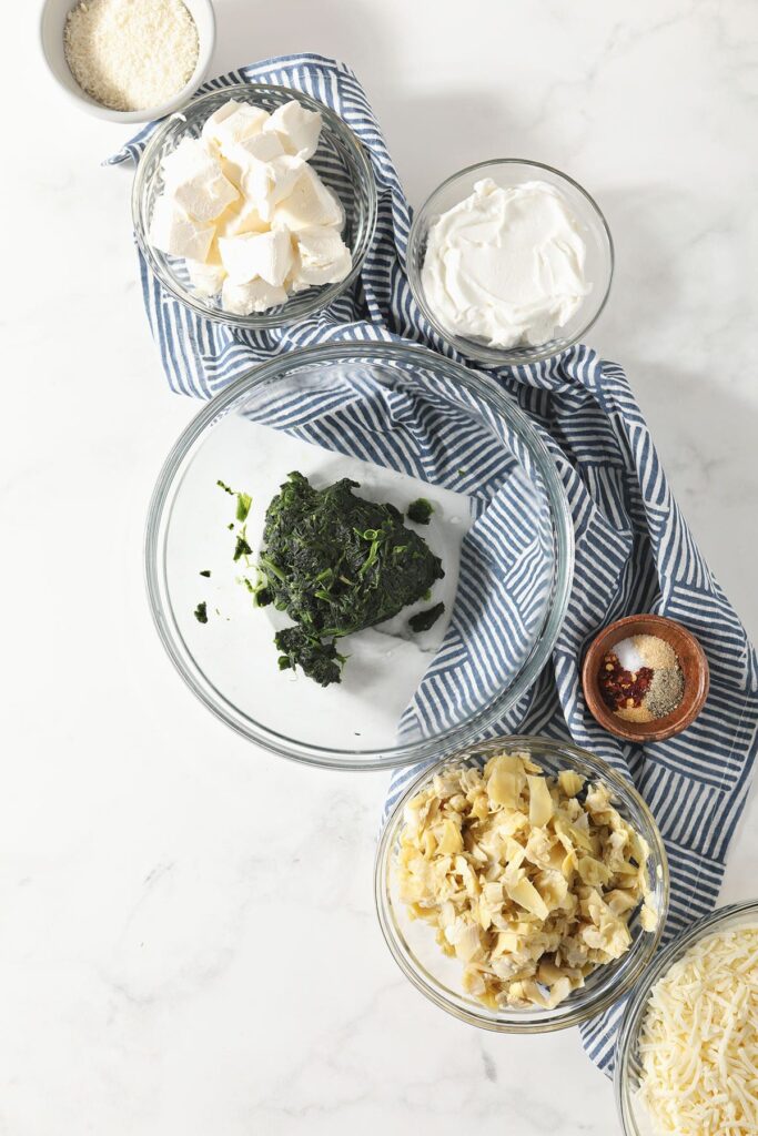 Ingredients to make spinach dip with artichokes in bowls on marble