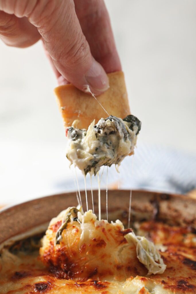 A pita chip scoops up hot Spinach Artichoke Dip