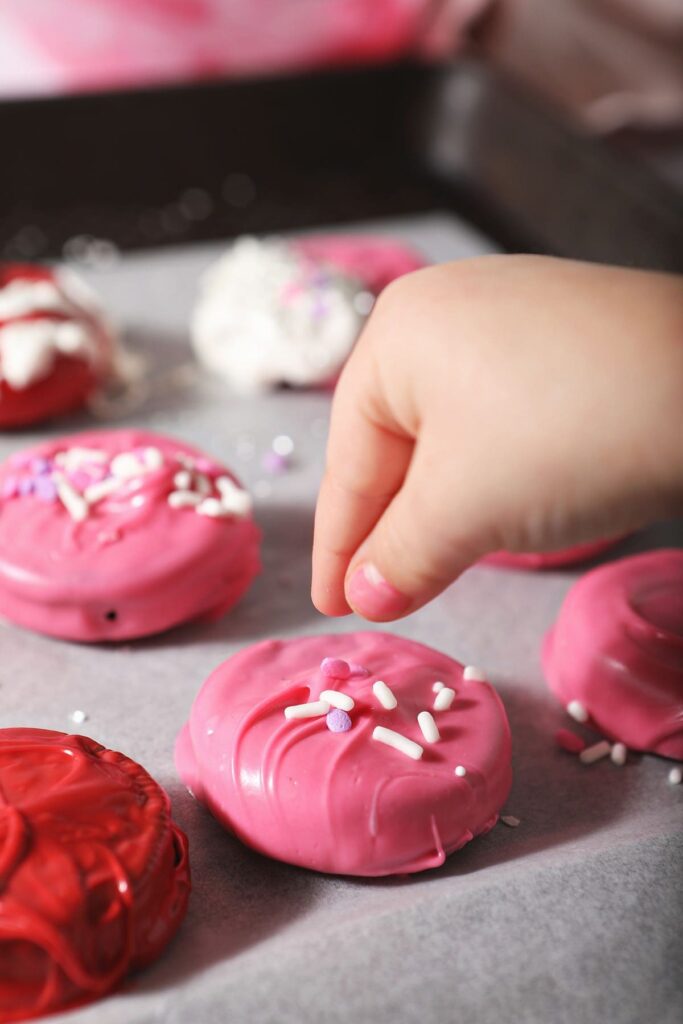 A child drops sprinkles onto a pink Oreo