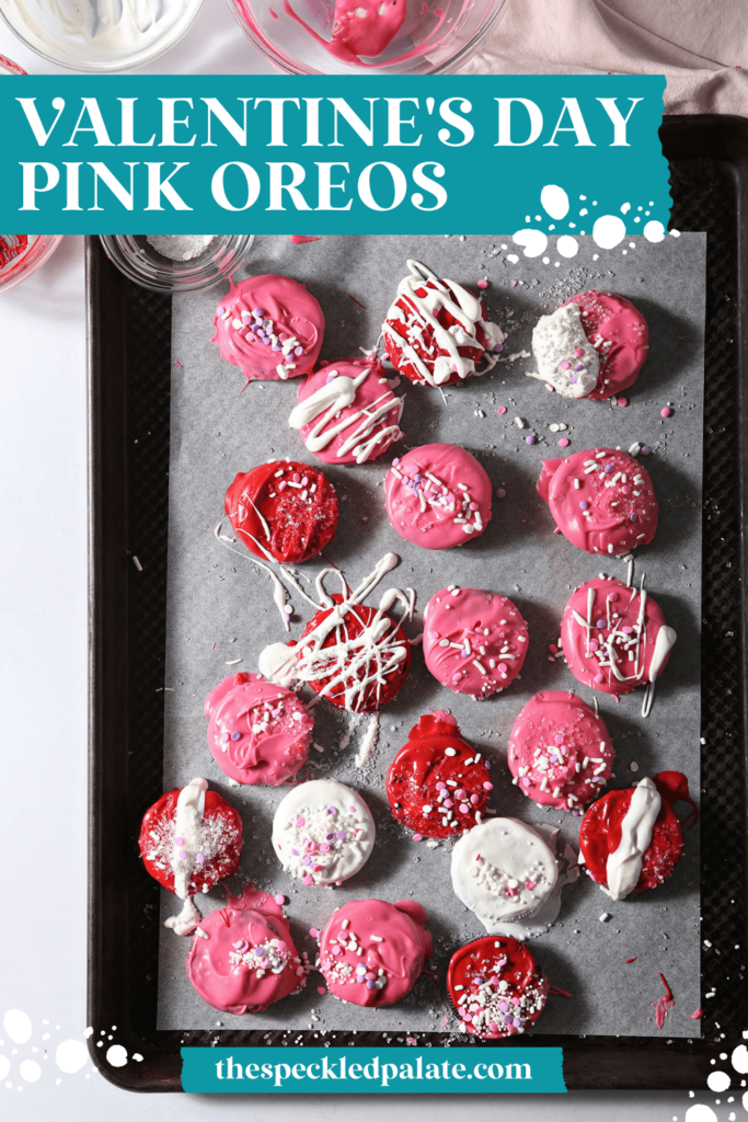 A sheet pan holding pink, red and white decorated chocolate-dipped Oreos with the text Valentine's Day Pink Oreos