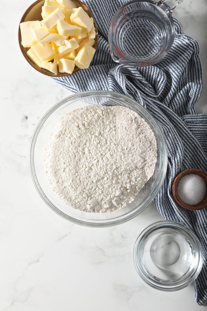 Ingredients to make Whole Wheat Pie Crust in bowls on a blue towel