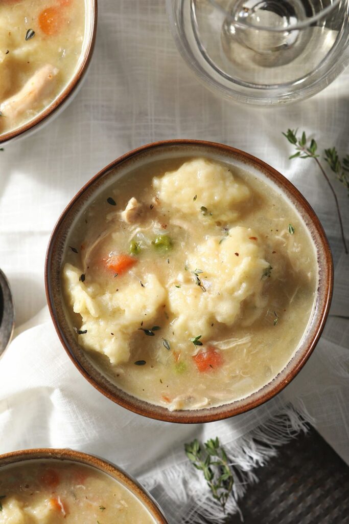 Three bowls of Dutch Oven Chicken and Dumplings next to a glass of wine