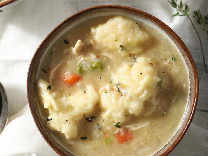 Three bowls of Dutch Oven Chicken and Dumplings next to a glass of wine