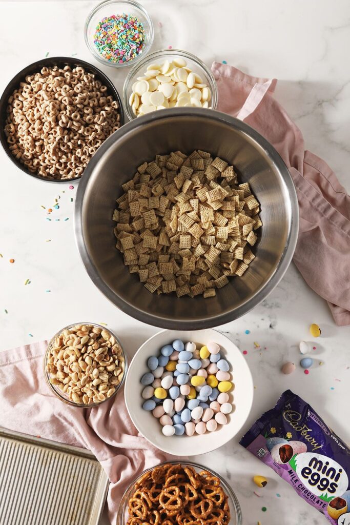 Ingredients to make a white chocolate chex mix for easter in bowls on marble