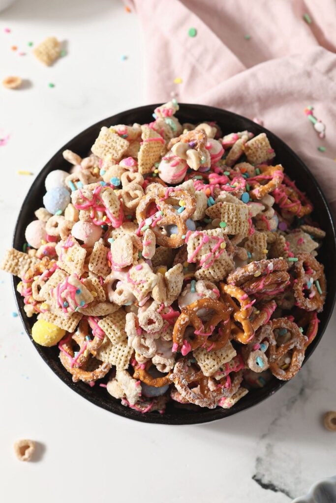 A bowl of sweet and salty chex mix on marble with a pink linen