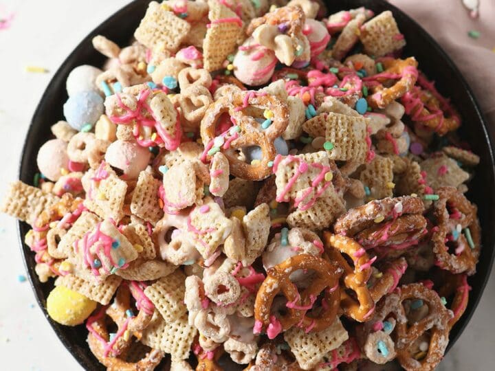 A bowl of sweet and salty chex mix on marble with a pink linen